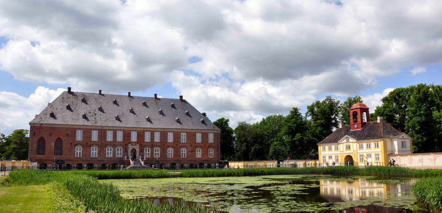 Valdemars Slot hovedbygning og porthus på en sommerdag med overskyet himmel. I forgrunden ses gårdspladsens vandbassin.