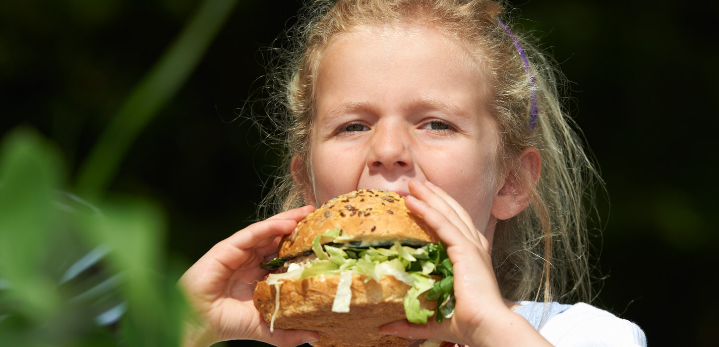 En pige tager en stor mundfuld af en burger.