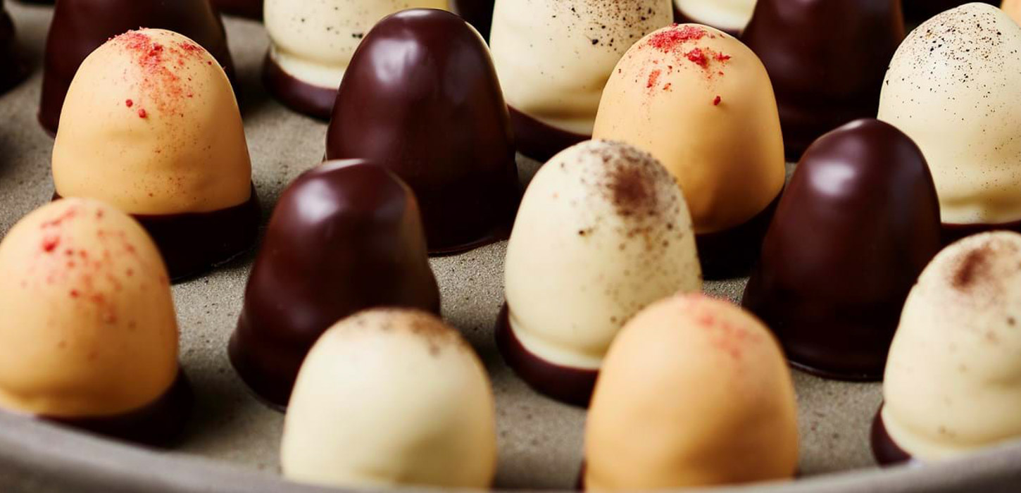 Nærbillede af små, delikate flødeboller; mørke, hvide med mørkt drys og ravfarvede med rødligt drys.