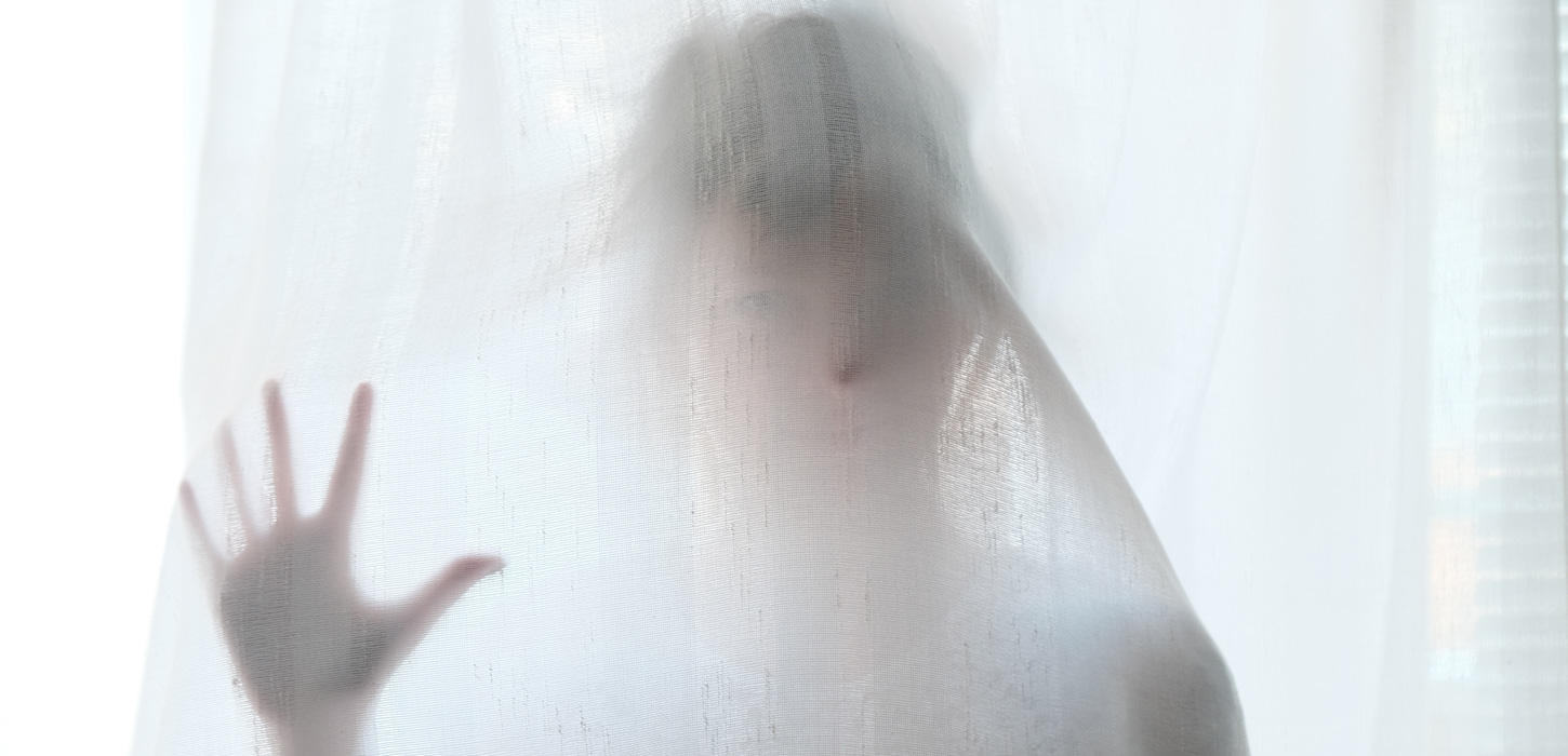 Spøgelseslignende form ses bag et hvidt gardin.