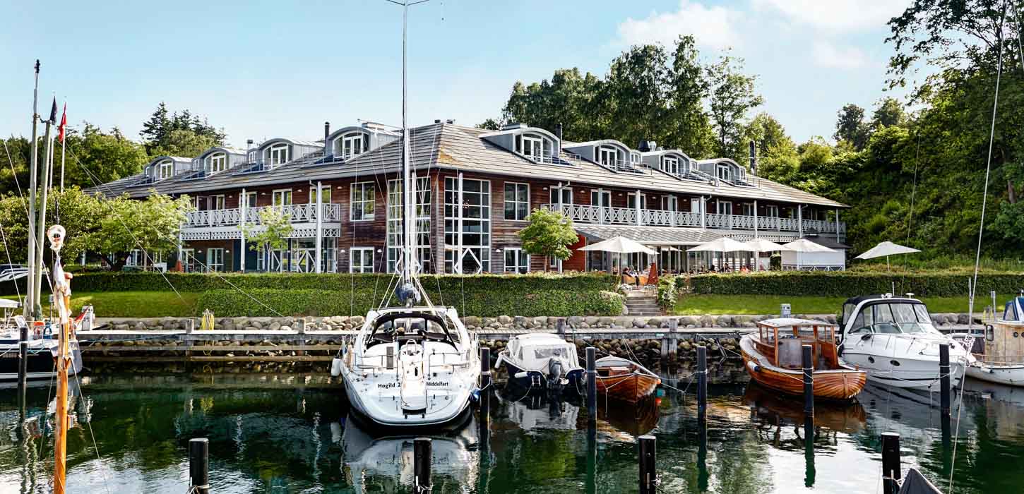 Stor, prangende rød bygning med hvide vinduer og hvide altaner, der ligger ud til en bådehavn.