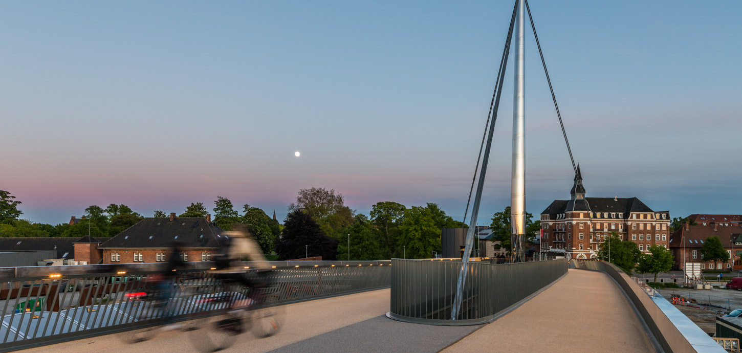 Cyklist på Byens Bro i Odense. I baggrunden ses smukke farver på aftenhimmelen og byens huse og tage.