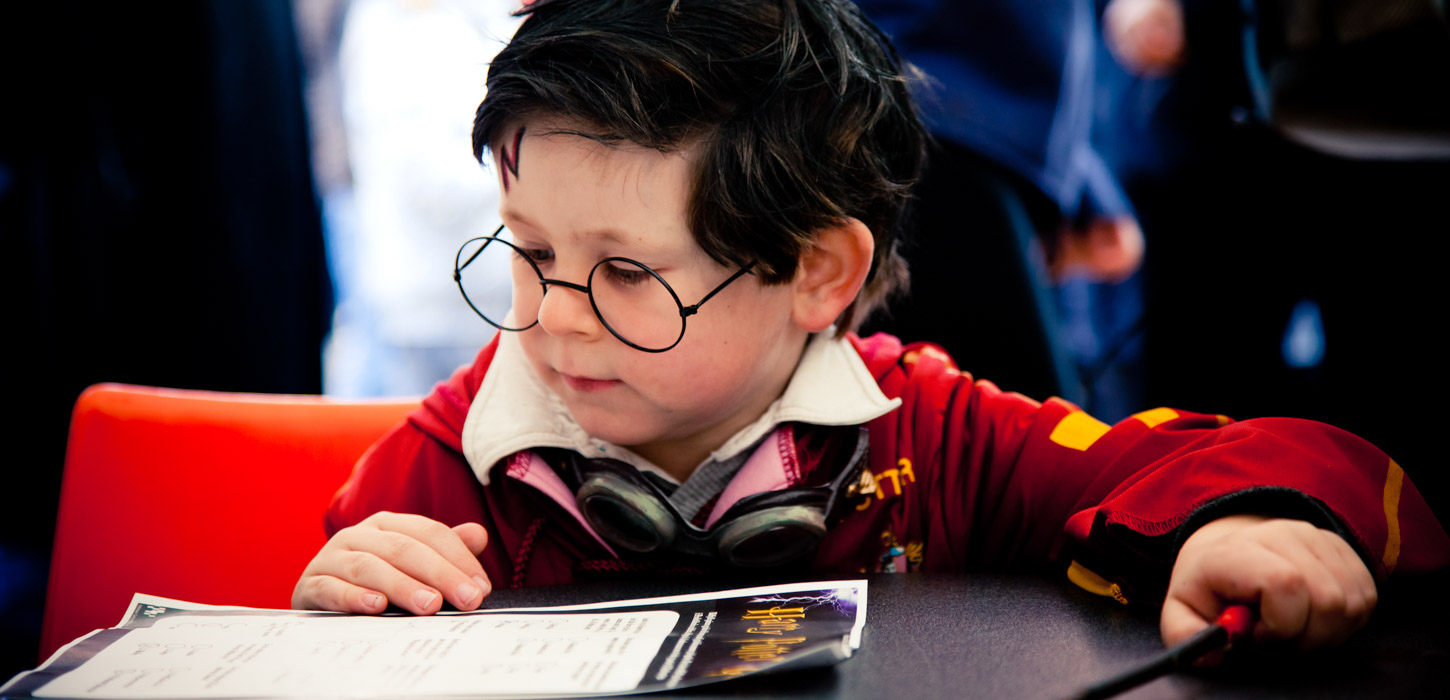 Dreng udklædt som Harry Potter til sidder og kigger på et stykke papir der ligger på bordet foran ham.