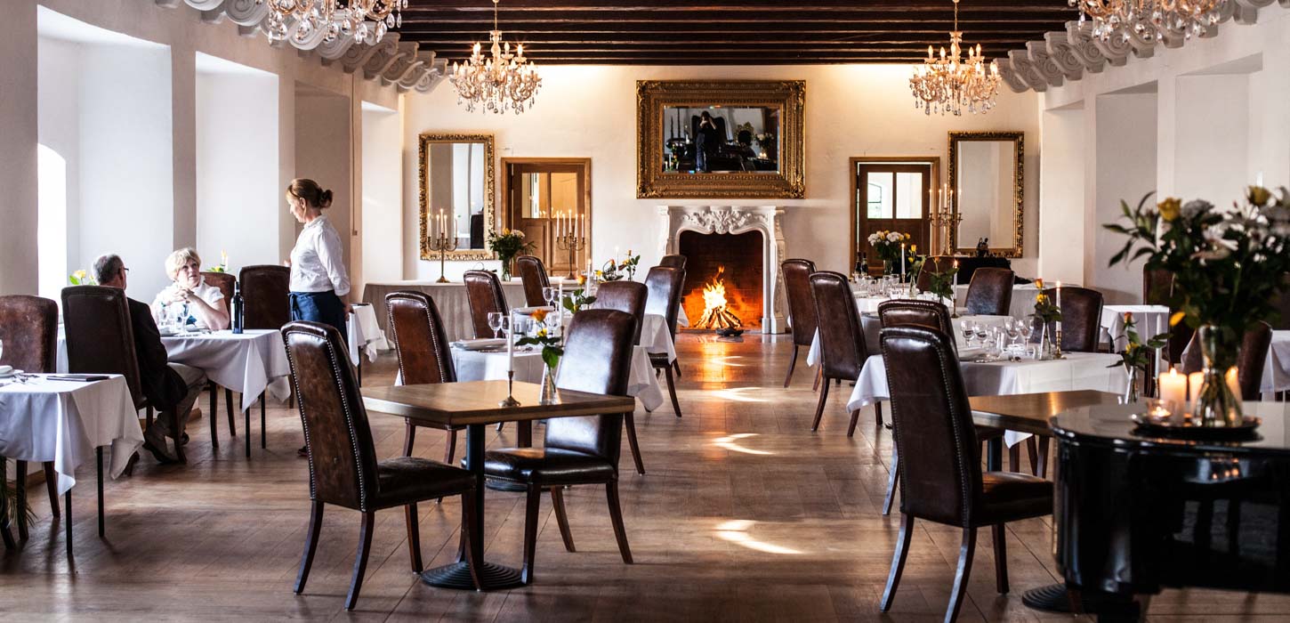 Stor, flot riddersal på en restaurant. Et par bliver serviceret ved en vinduesplads.