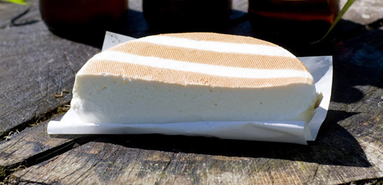 Nærbillede af en halv rygeost på hvidt papir på et træbord.