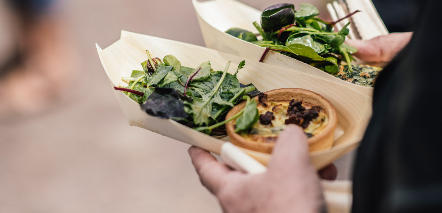 Hånd holder snack-bakker med quiche og salat.