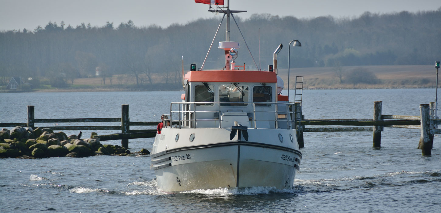 Båd i vandet ved Bjørnø. Bagved ses pæle og hegn ude i vandet, og i baggrunden ses land.