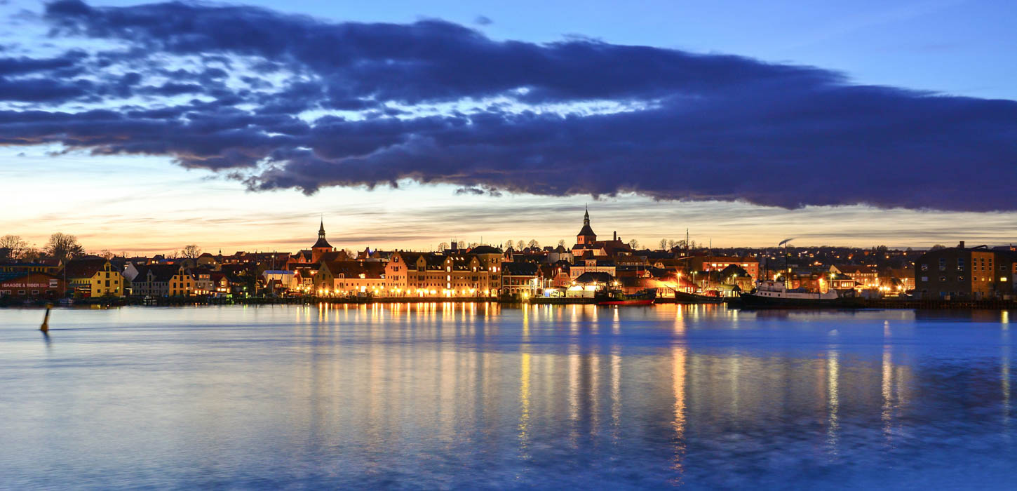 Udsigt over Svendborg Havn under en stor, mørkeblå sky med hyggelige lys fra byen.