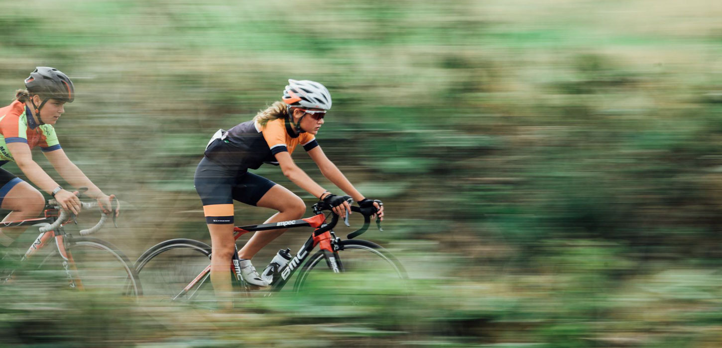 To kvindelige cykelryttere i fuld fart gennem grønt landskab.
