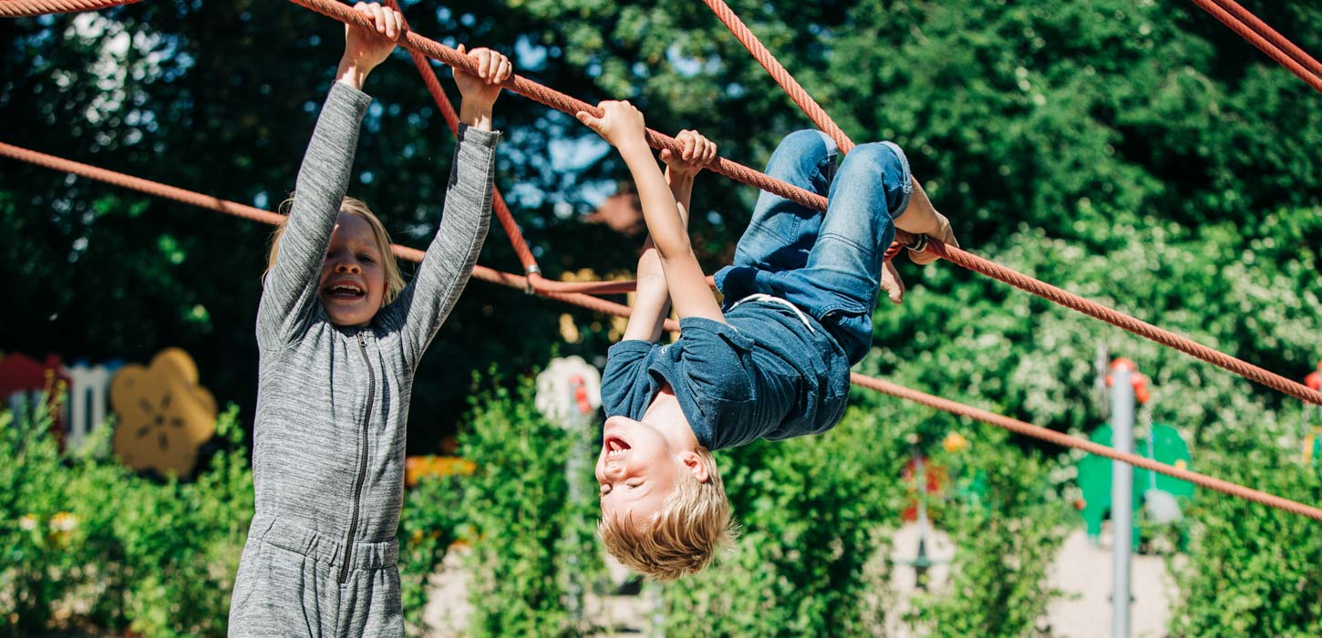 To storgrinende børn, der hænger i et klatrestativ på en legeplads.