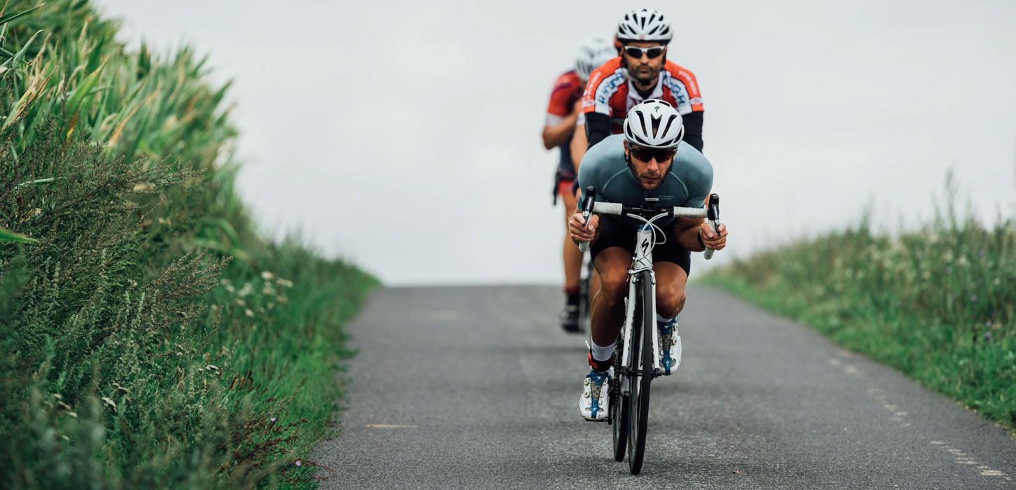 Tre foroverbøjede cykelryttere på ved ned ad bakke.
