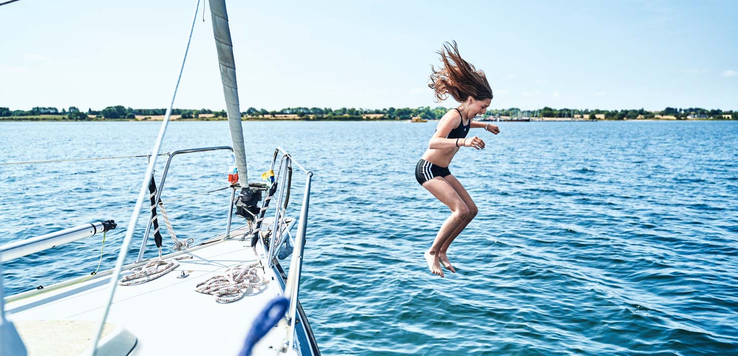 Pige midt i et hop fra båd. Det er sommer, havet er blåt og solen skinner.