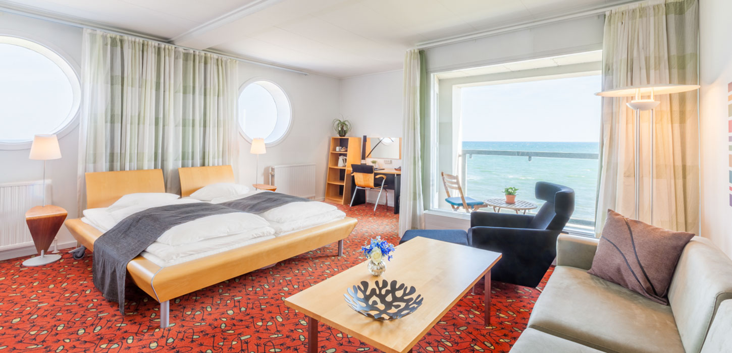 Hotelværelse med stor dobbeltseng og afslapningshjørne, med udsigt over havet.