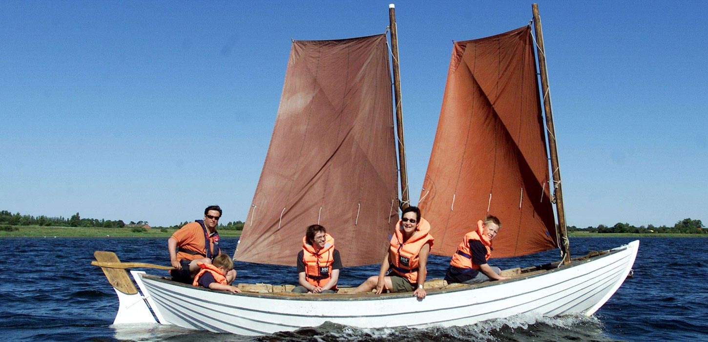 Familie med redningsveste sidder i en smakkejolle på vandet.