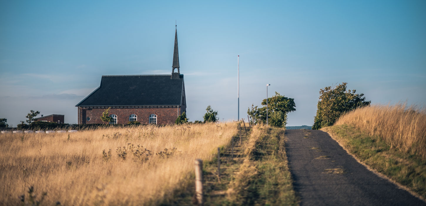 Landevej omringet af marker i varme farver og med en kirke i baggrunden.