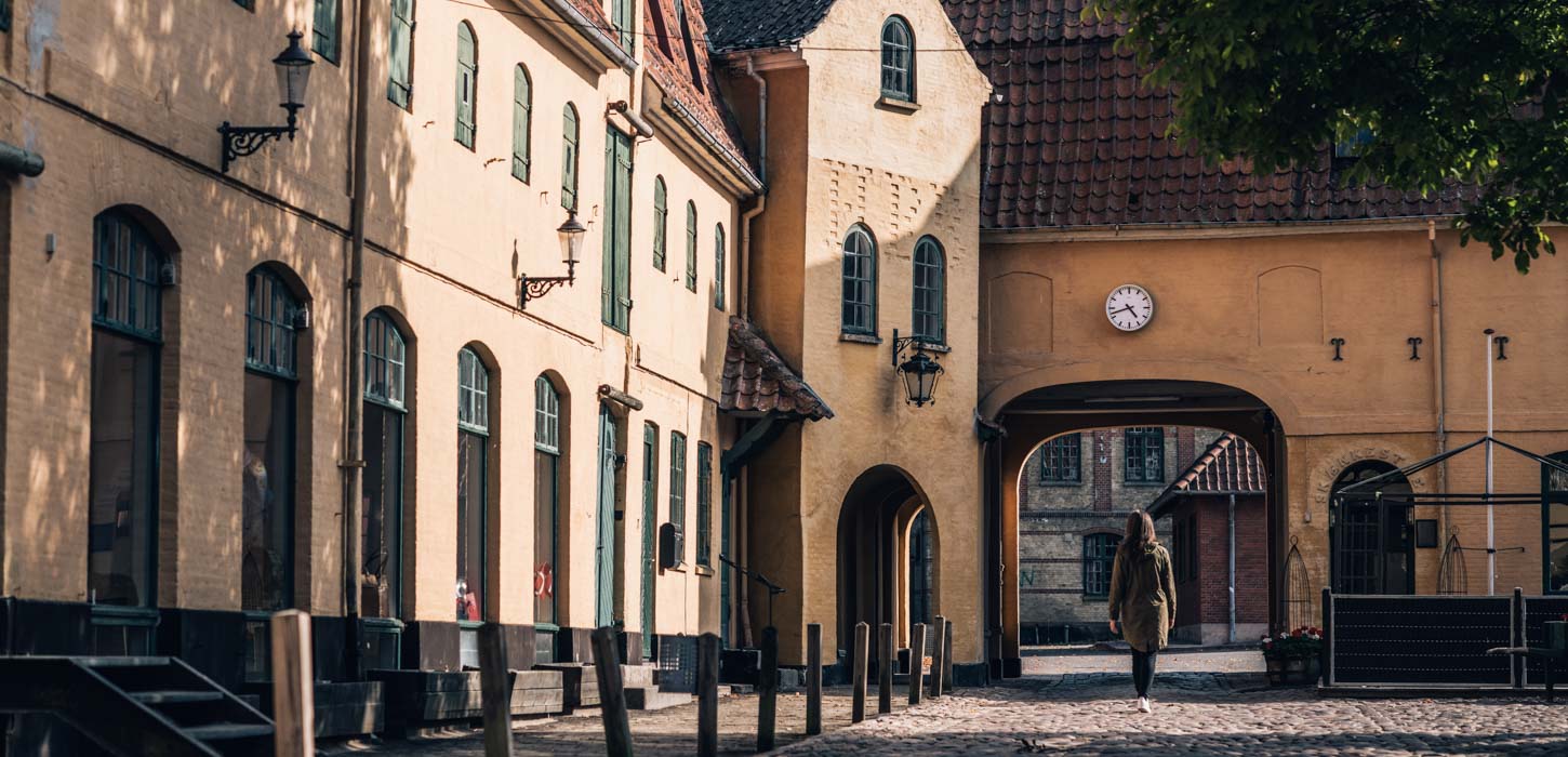 Kvinde på vej ind gennem port i gammel bygning i Assens. Uret over porten viser, at klokken er 17.45.