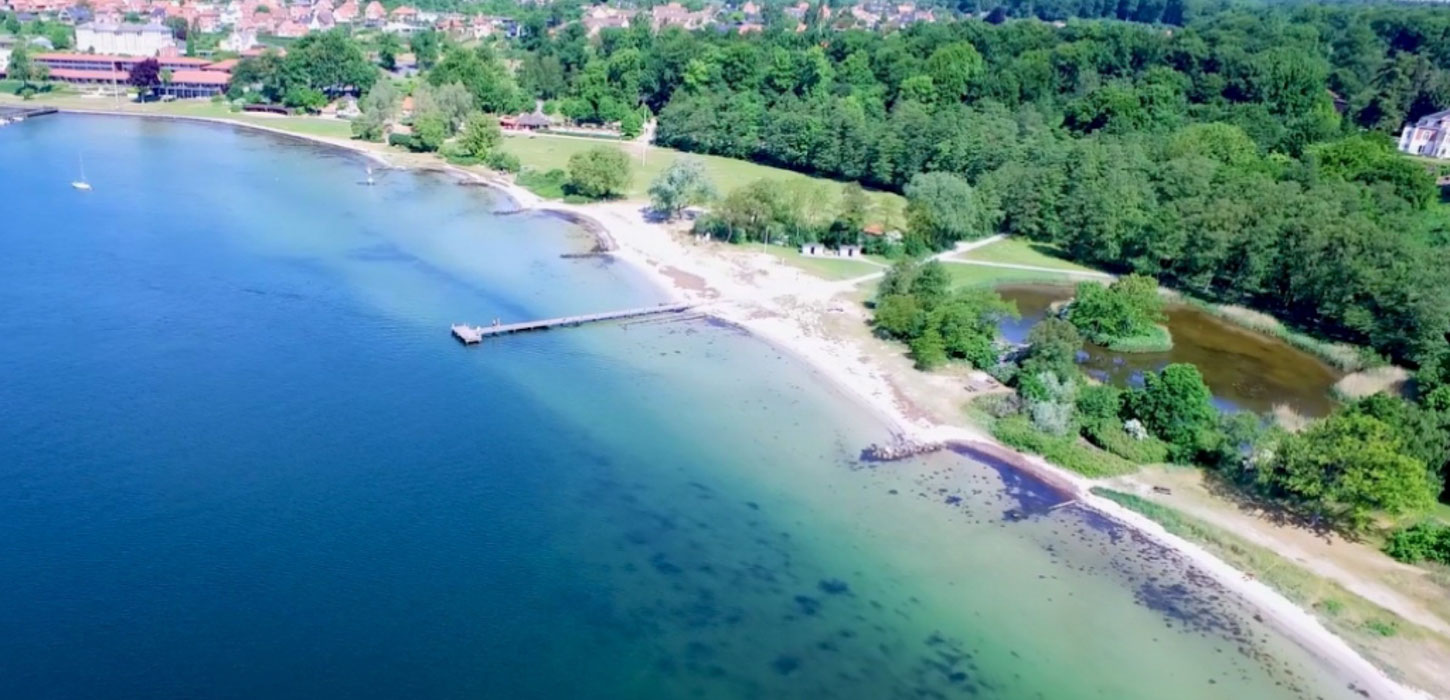 Strand set ovenfra med lyst sand og blåt og turkis vand.