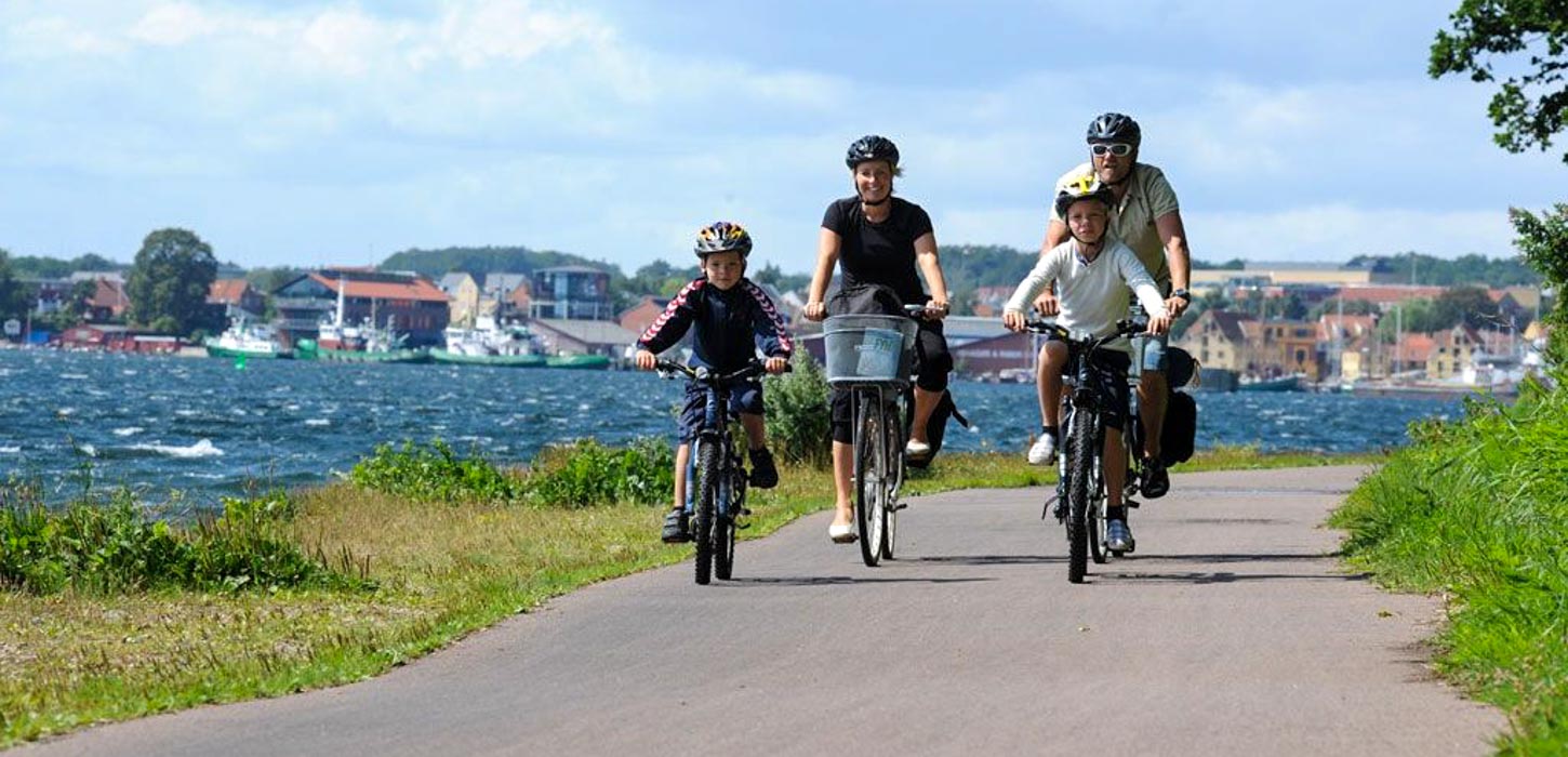 Familie på to voksne og to børn cykler langs kysten på Thurø.