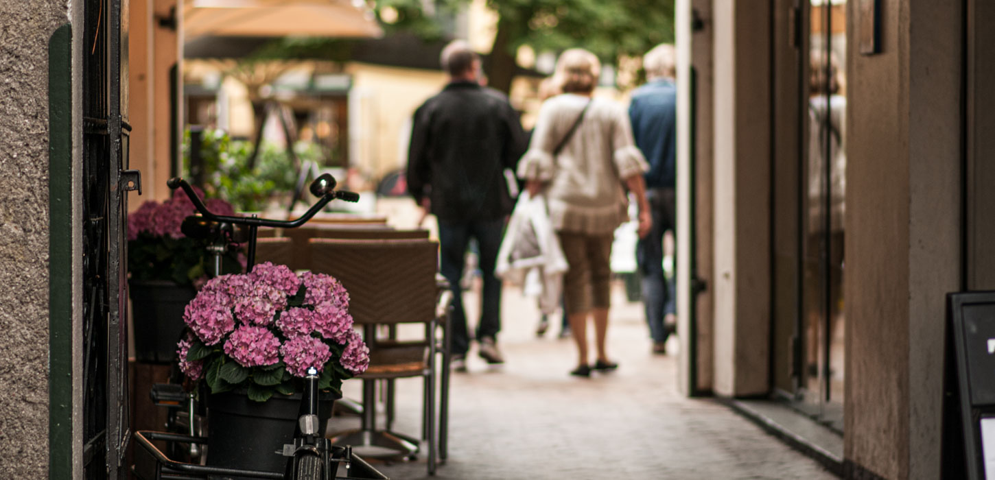 Hyggelig gågade med mennesker og lyserøde blomster i forgrunden.
