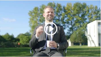 Mand sidder i jakkesæt med en kaffekop udenfor.