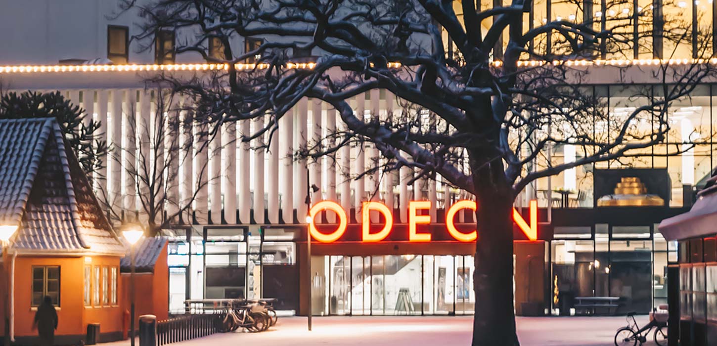 Odeon om aftenen set udefra foran hovedindgangen. Ovenover hovedindgangen er 'Odeon' oplyst med orange lys.