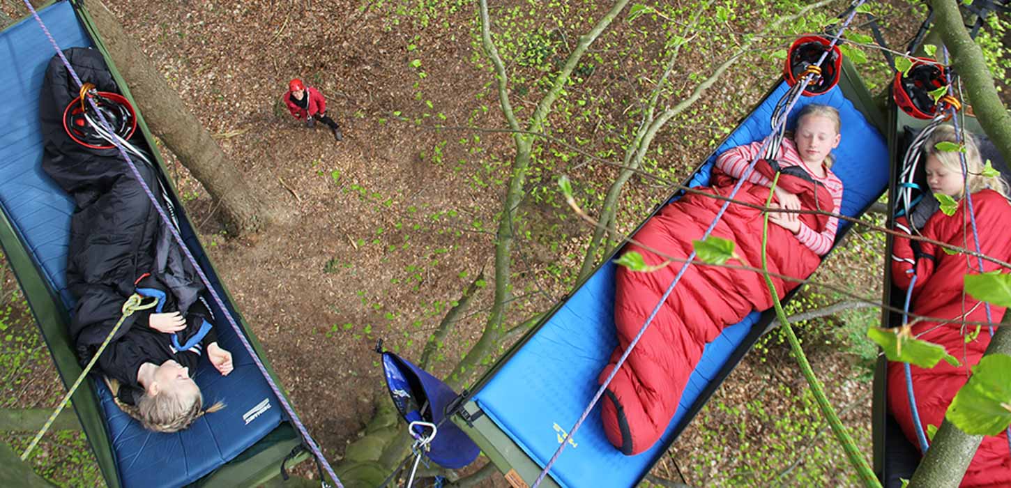 Tre børn ligger og sover under åben himmel i soveposer