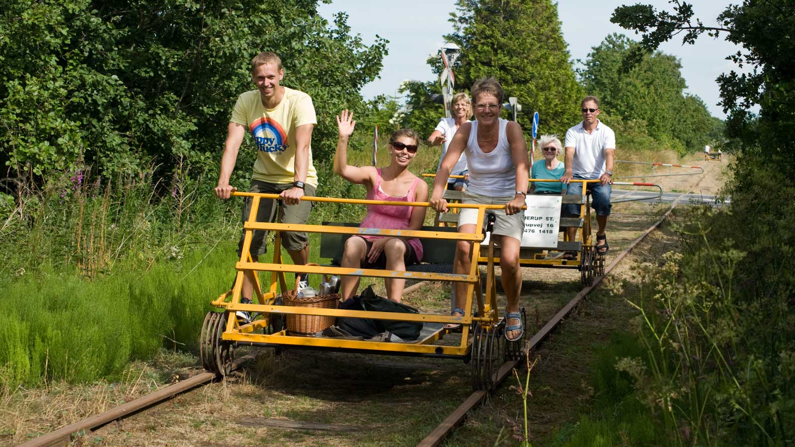 En flok mennesker kommer kørende på to skinnecykler og smiler og vinker til kameraet.