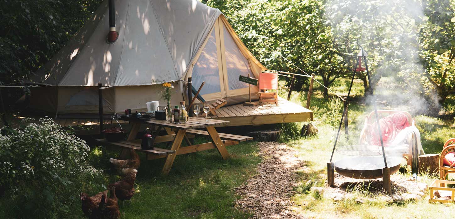 Glampingtelt i grønne omgivelser med et bål tændt ude foran.