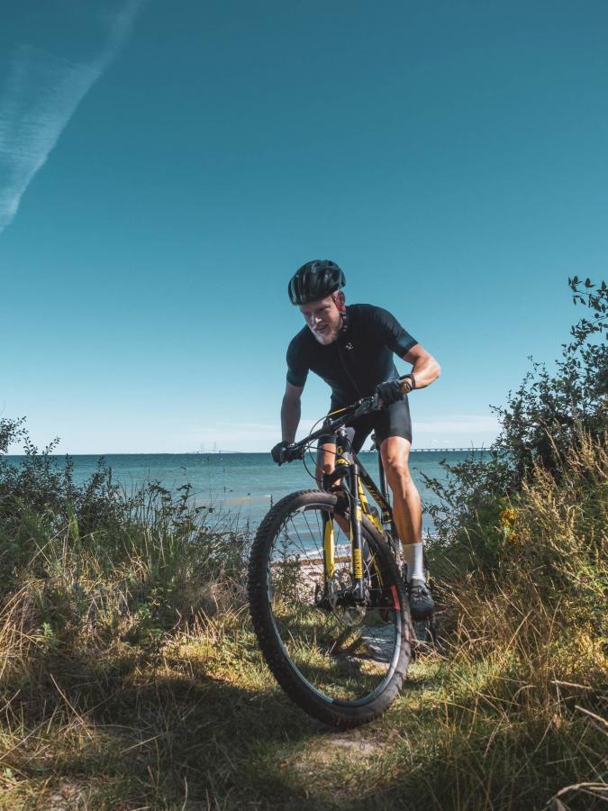 Person på cykel på vej op ad stejl skrænt med havet i baggrunden.