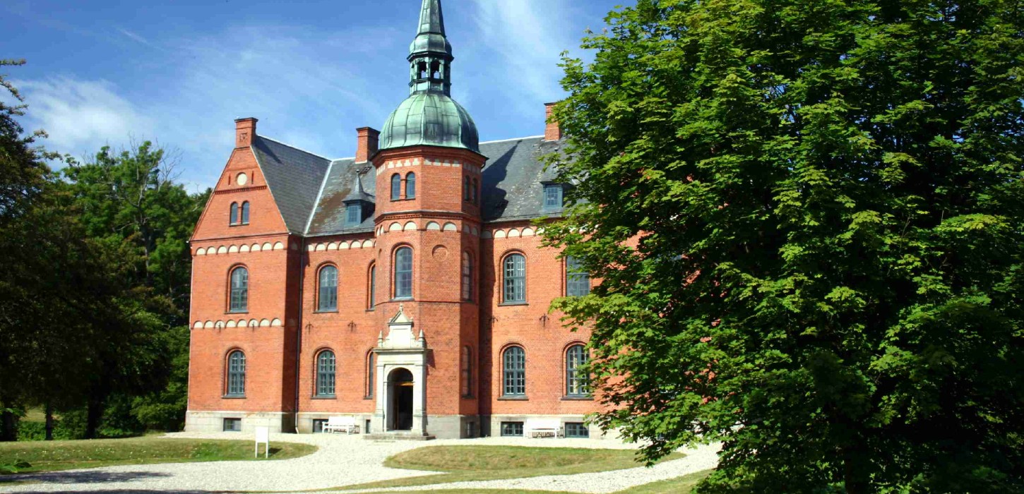 Stort, rødt slot med kobbertop og et fyldigt grønt træ til højre.