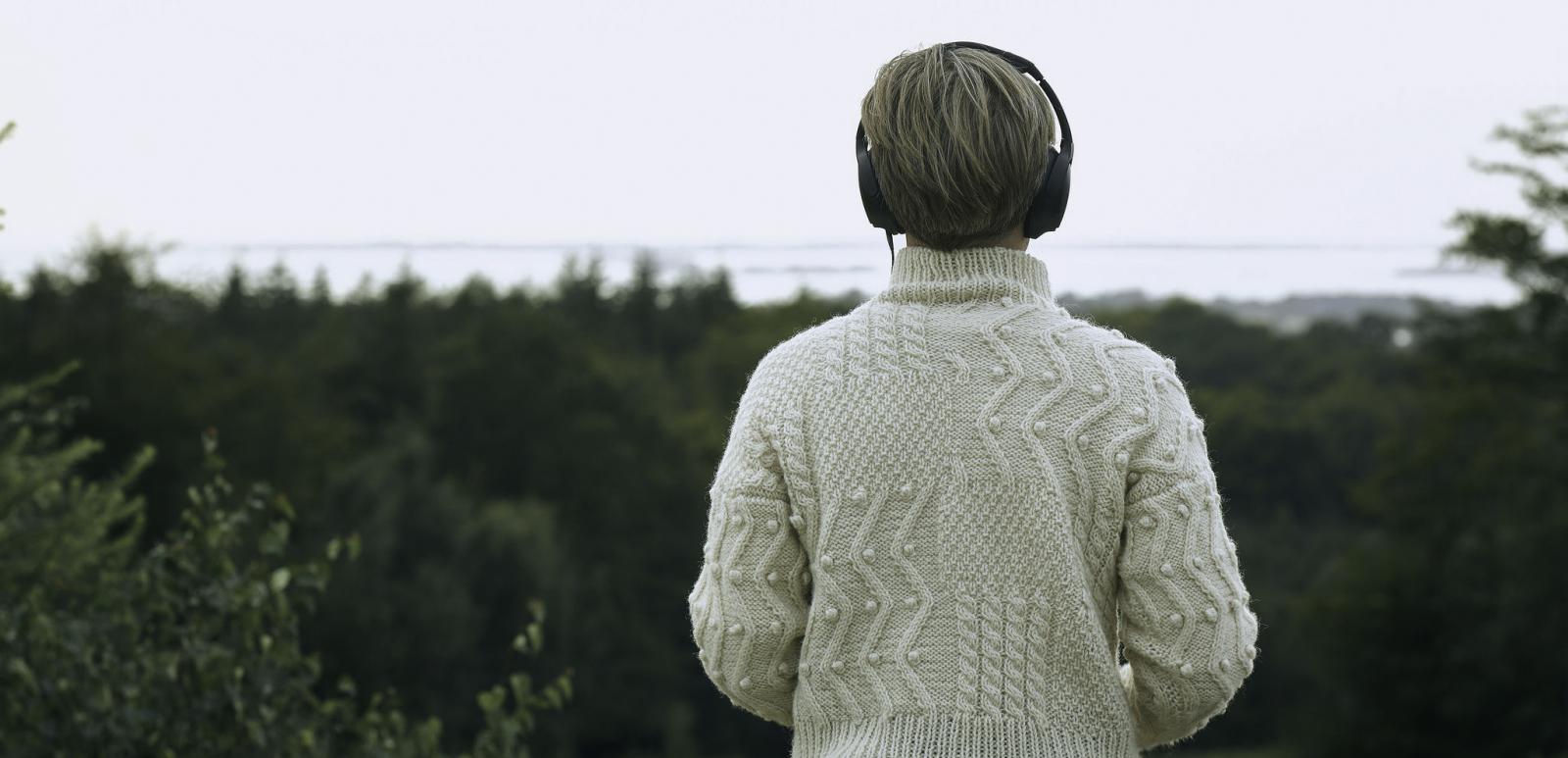 Person, der kigger ud over naturen ses bagfra med høretelefoner på
