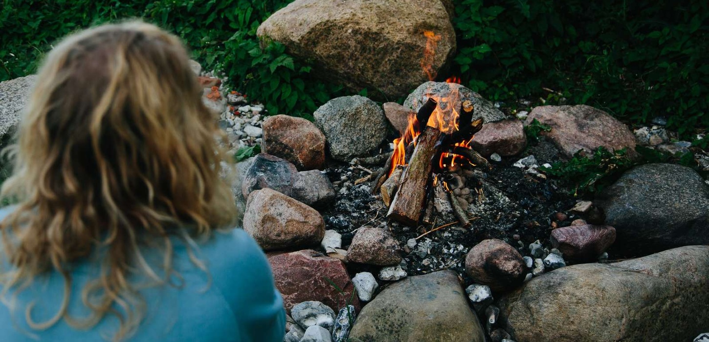 Kvinde sidder med ryggen til og kigger på et bål.