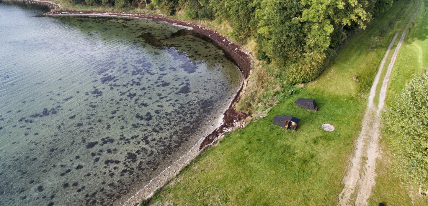 To shelters set fra oven. De ligger lige ud til vandet i smukke grønne omgivelser, og en markvej går lige forbi.