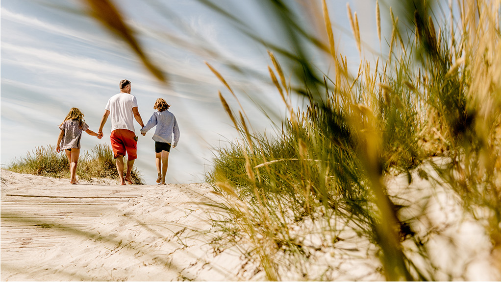 En familie går hånd i hånd på en strand.