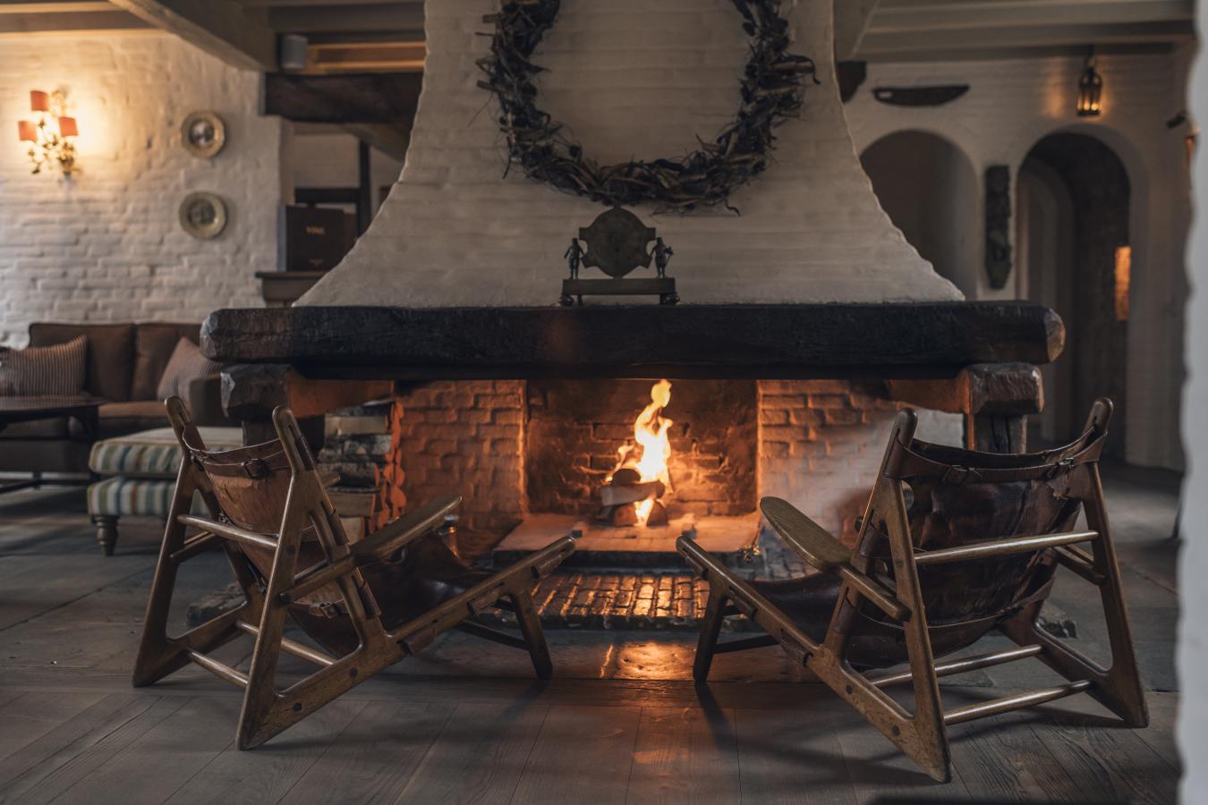 To tomme stole foran en åben kamin med ild i et rum med hvide murstensmure i aftenmørket.