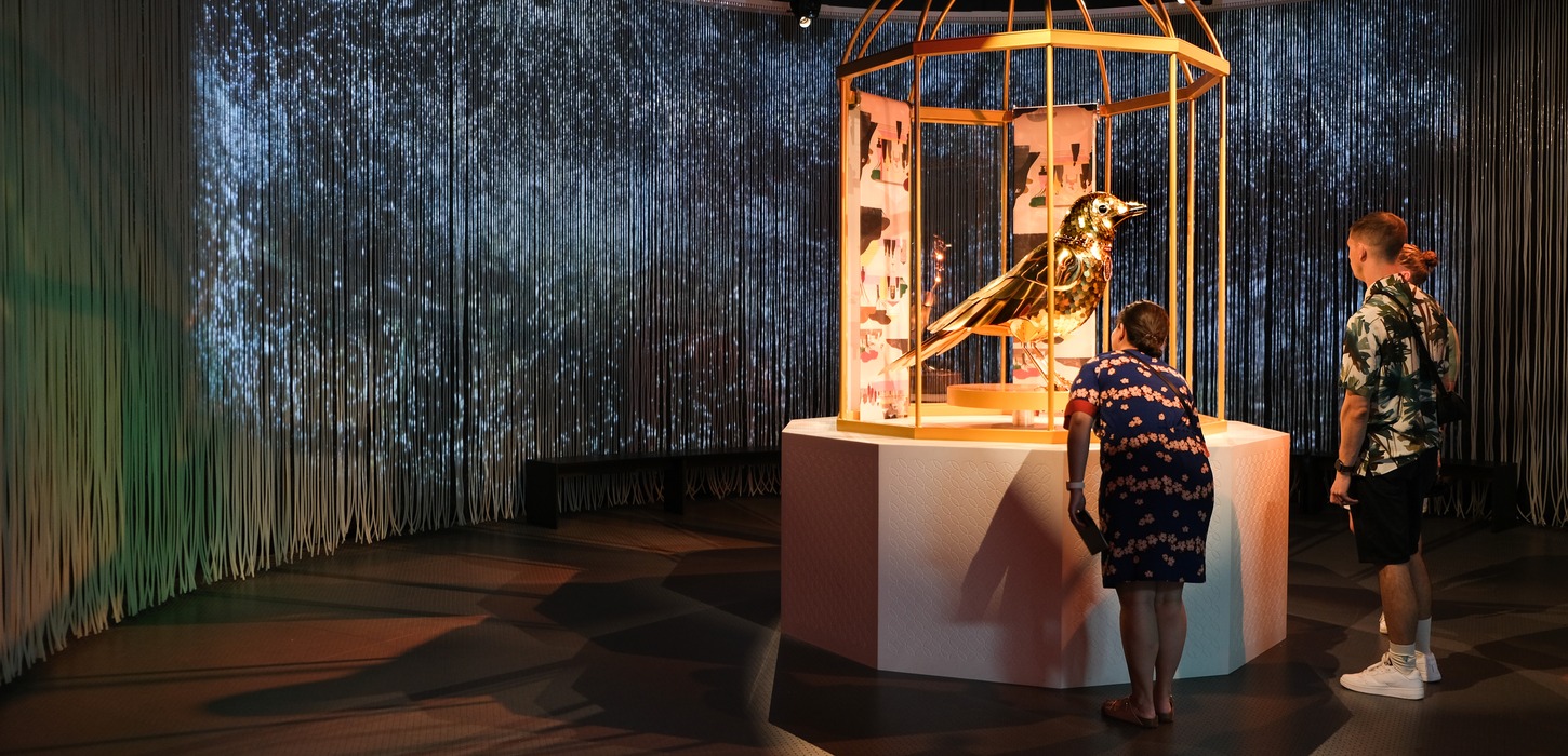 En familie kigger på skulptur af en stor guld nattergal i et guld bur på H.C. Andersens hus museum.