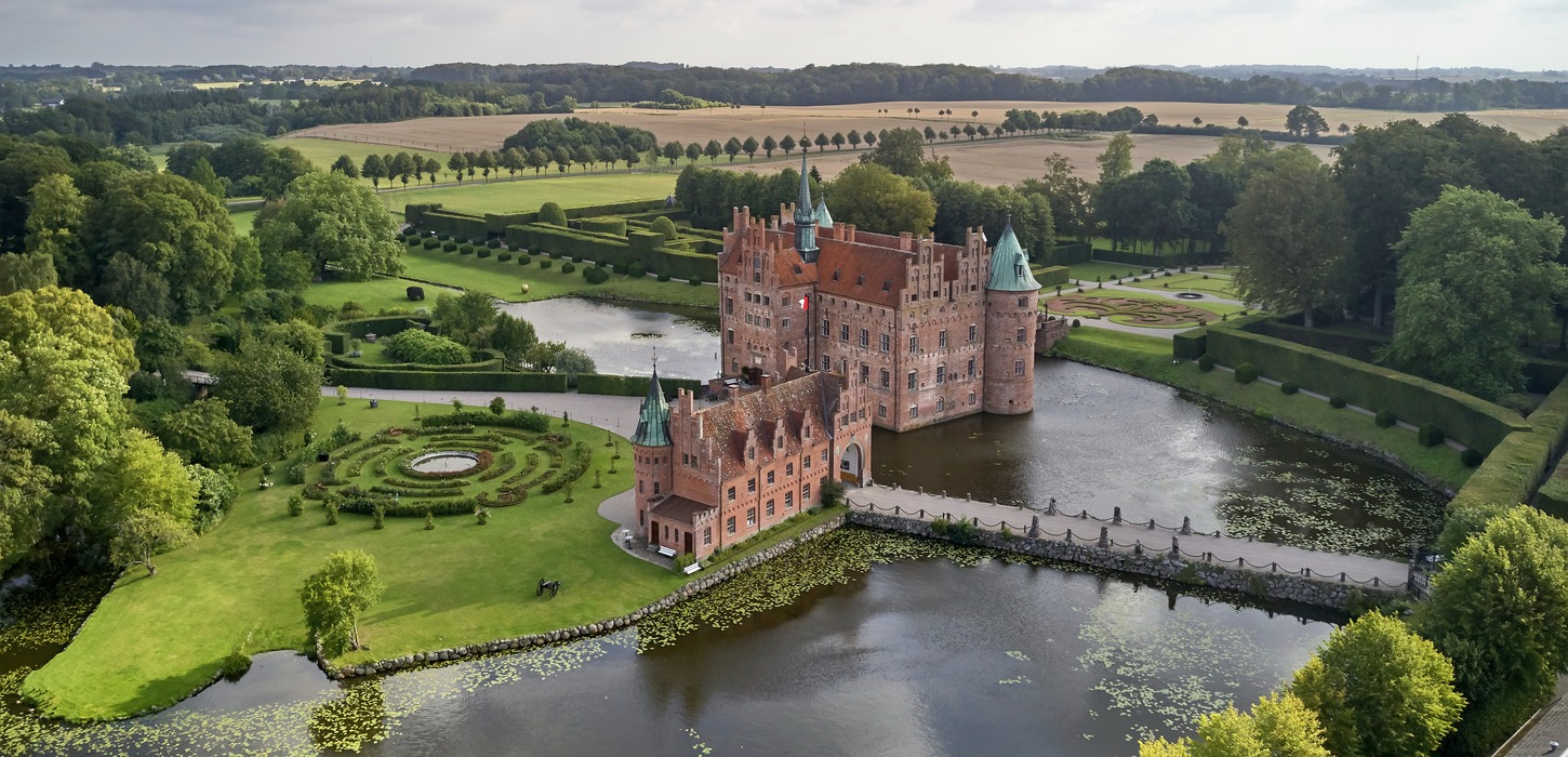 Egeskov Slot set oppefra med vand omkring og i grønne omgivelser.