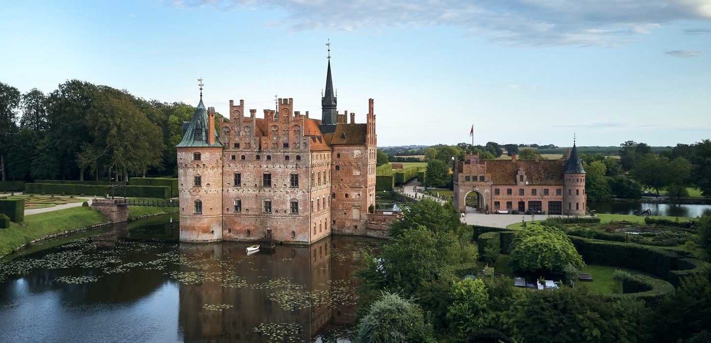 Egeskov Slot set fra oven med vandet foran og en åben blå himmel i baggrunden.