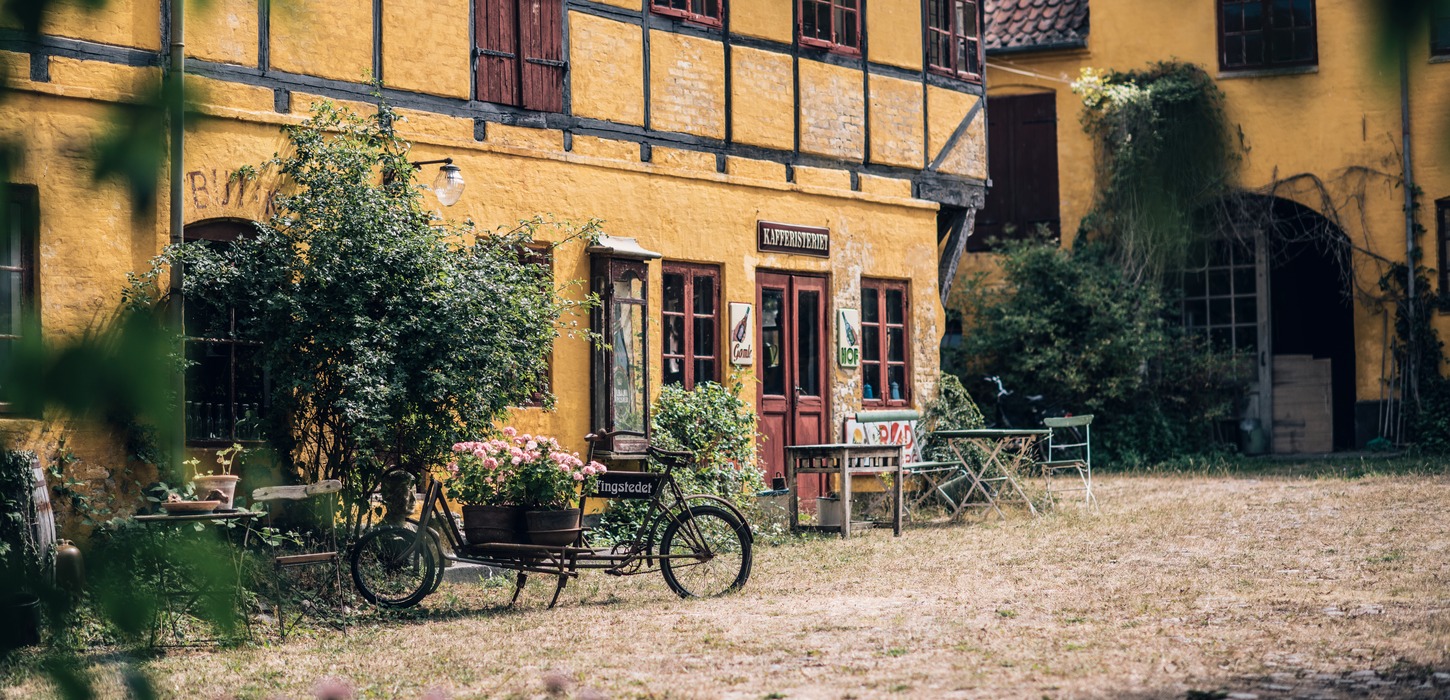 Hyggelig baggård med planter, borde, bænke og longjohn-cykler.