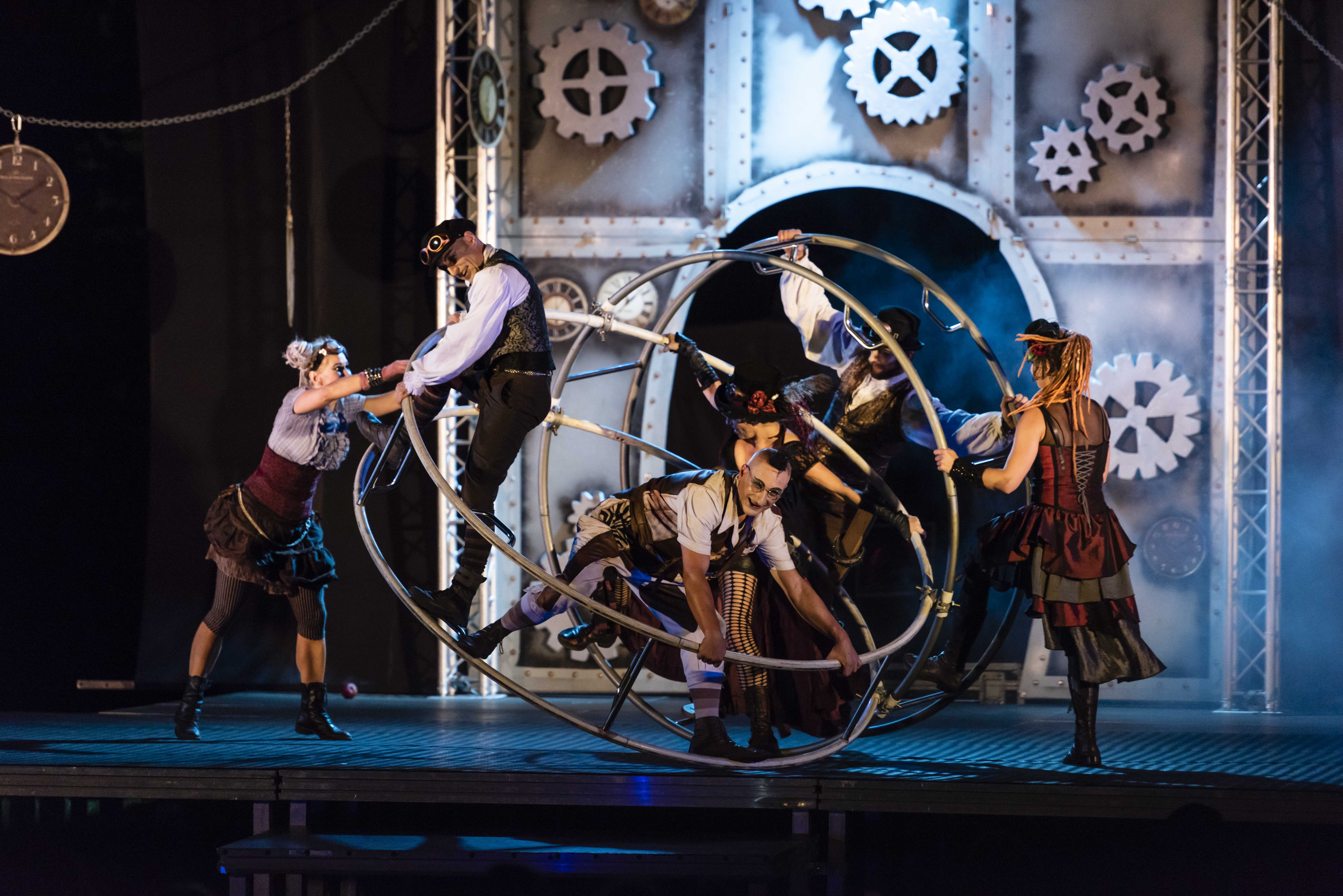 På en scene kravler to kvinder og tre mænd rundt på to store cirkusringe. 