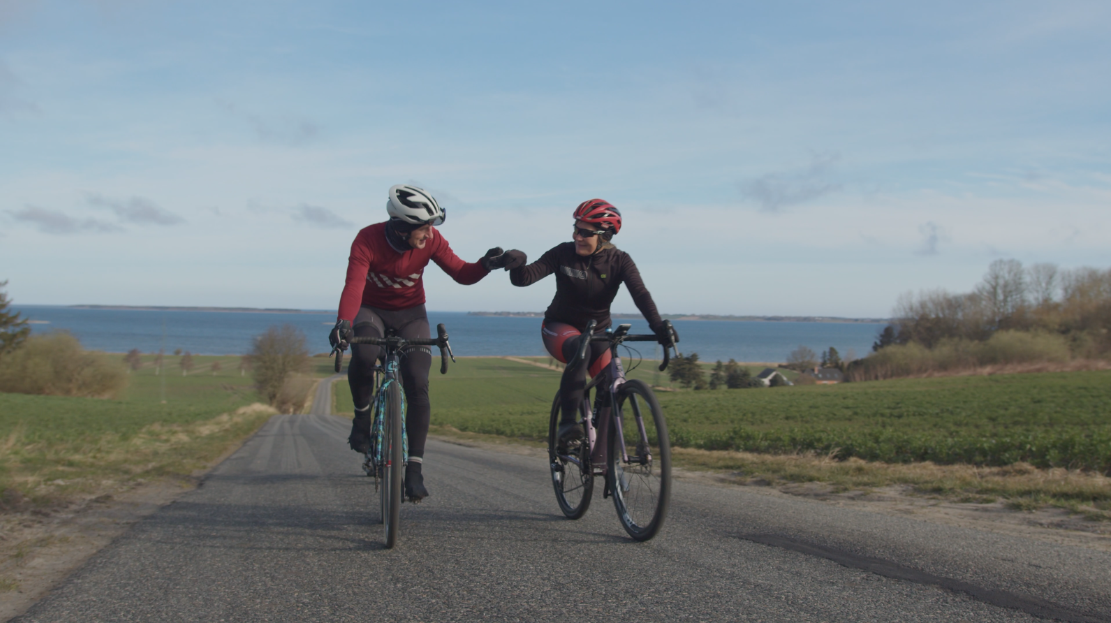Et par cykler op ad en bakke på landevejen og holder i hånd.