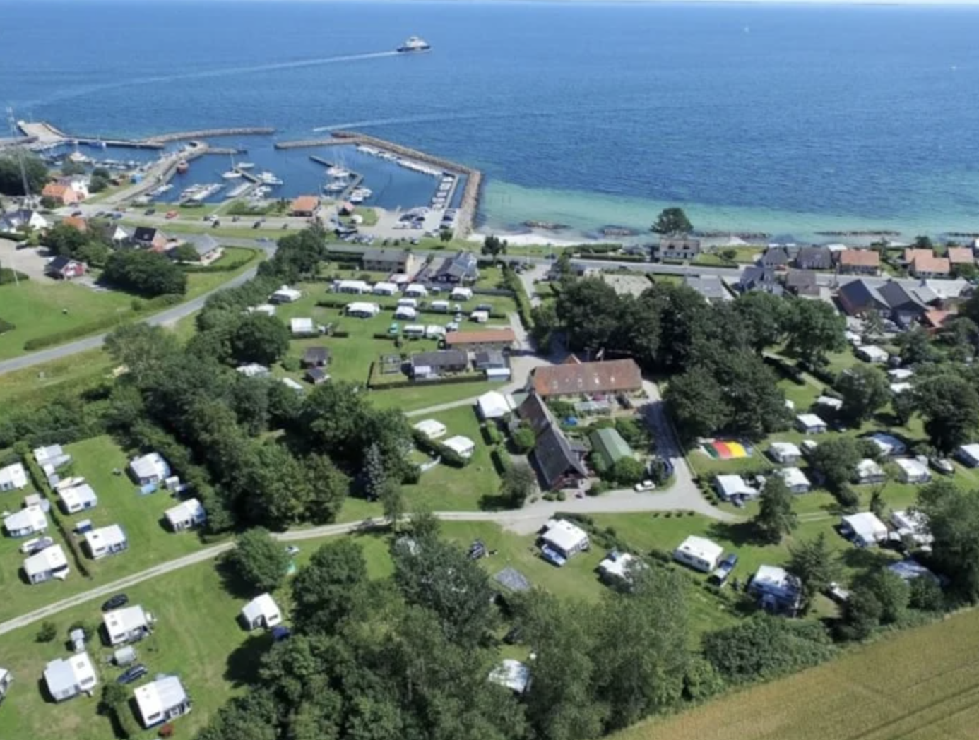 Færgegårdens Camping ses oppe fra i droneperspektiv. Man kan også se vandet og naturen.