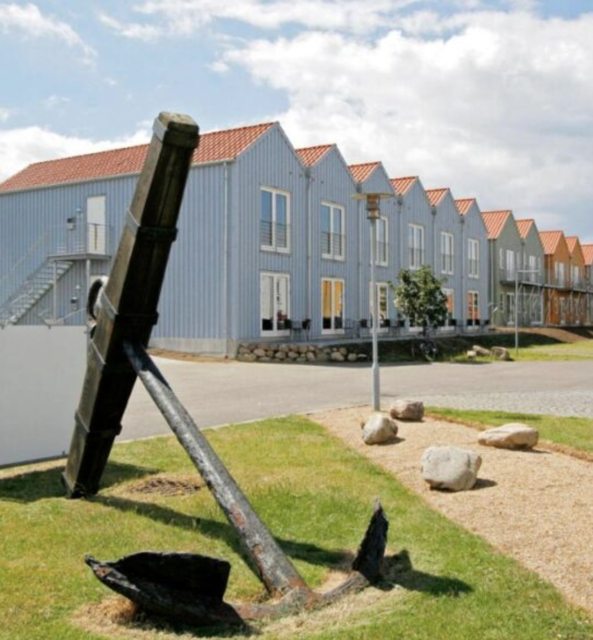 Viser de mangefarvede rækkehuse der udgør Rudkøbing Skudehavn. Foran ses et stort anker.