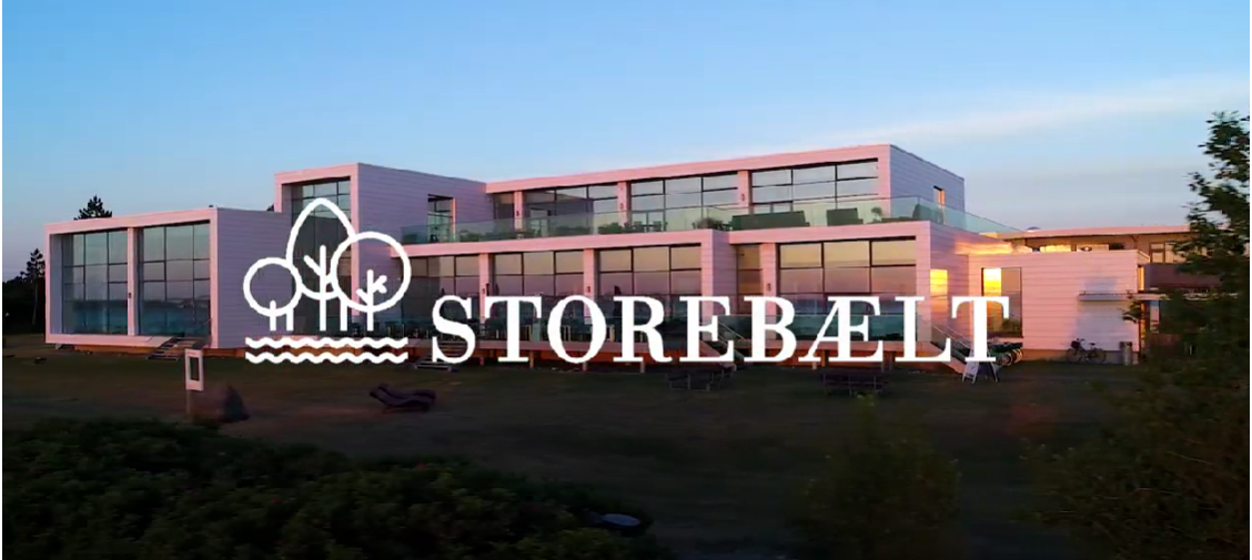 Hvidt hotel med store vinduer, der afspejler en solnedgang. Logo og teksten "Storebælt"