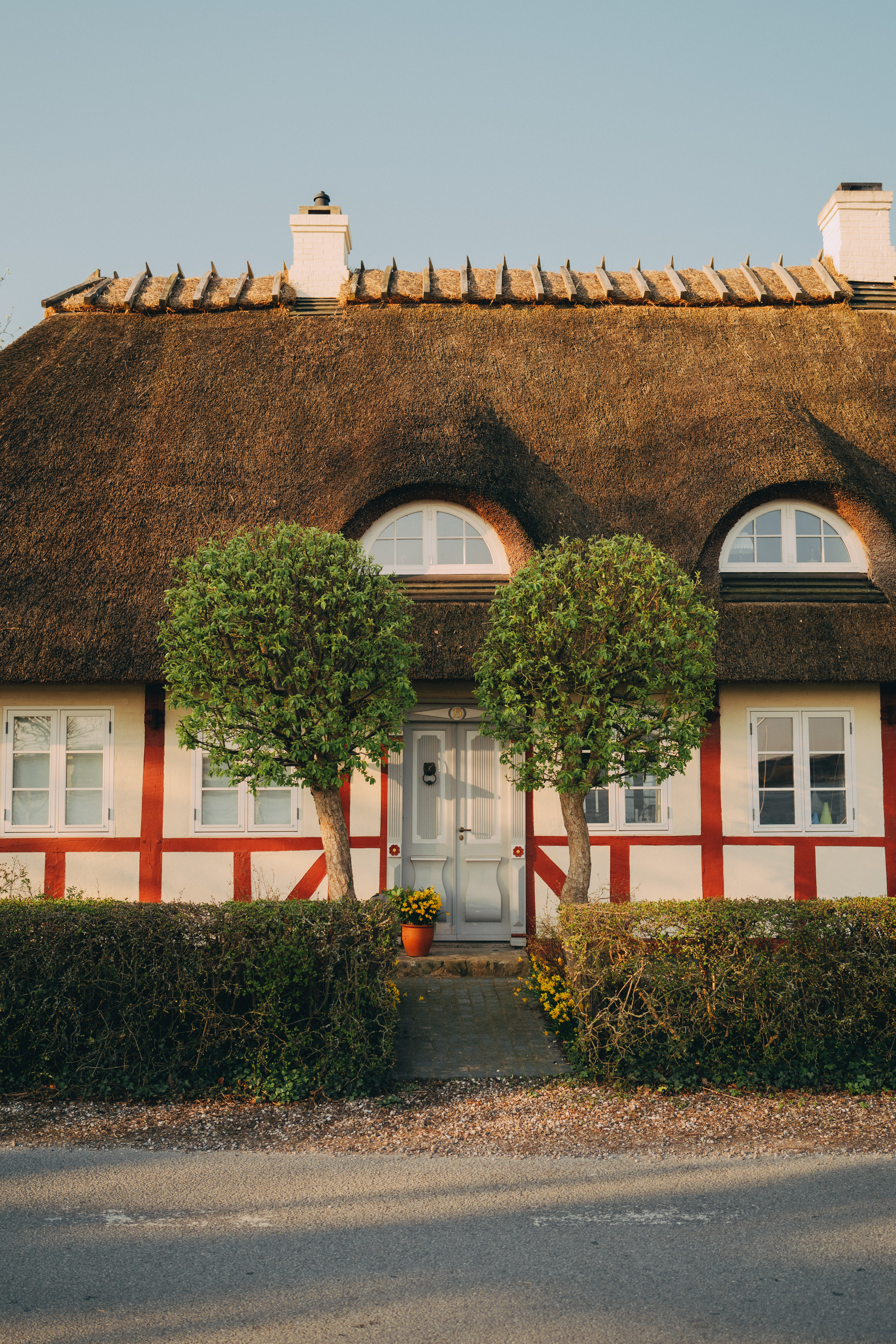 Hvidt og rødt bindingsværkshus med to veltrimmede buske foran hoveddøren.