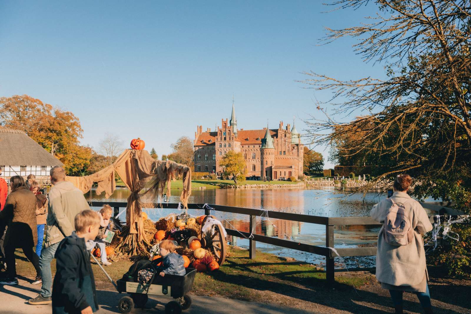 I baggrunden ses i Egeskov Slot omringet af vand. I forgrunden ses mennesker og halloween-pynt i form af græskar, spindelvæv og edderkopper.