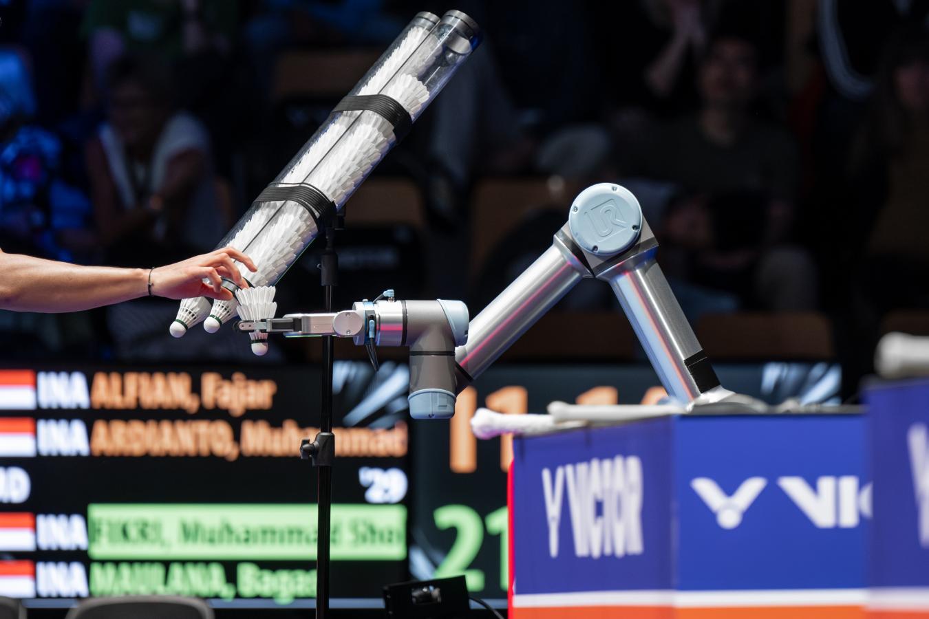 Arm rækker ind i billedet og tager fjerbold fra robotarm badmintonturneringen VICTOR Denmark Open 2023