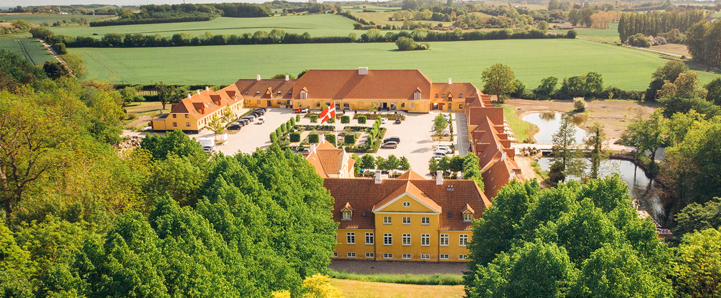 Et dronebillede af Broløkke Herregård med grønne marker og skov