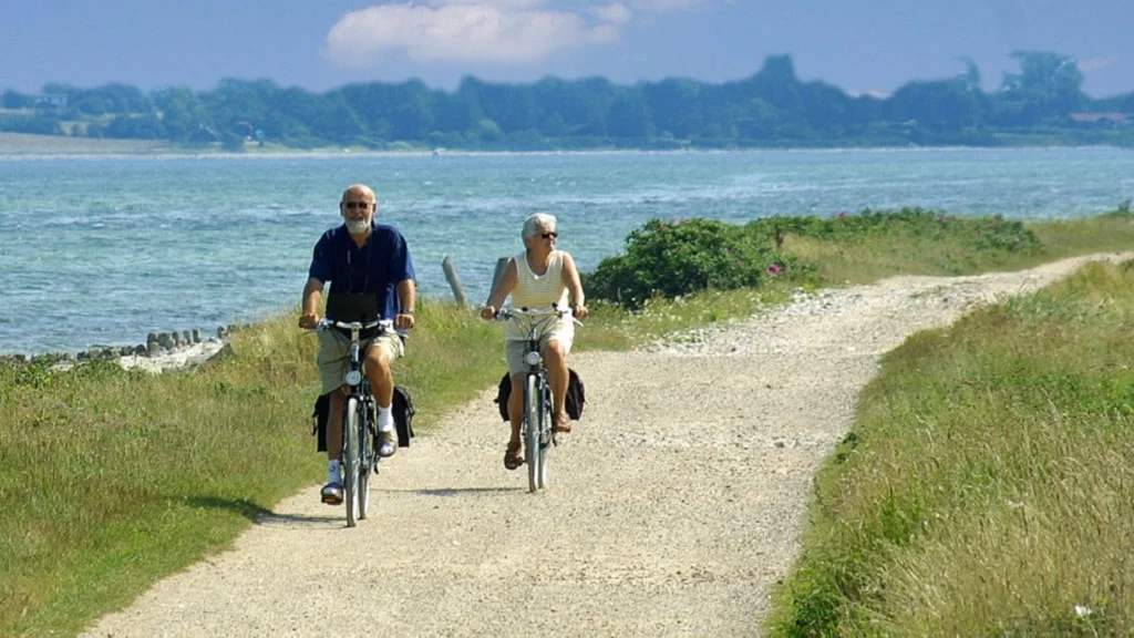 To personer cykler langs vandet på en sti.