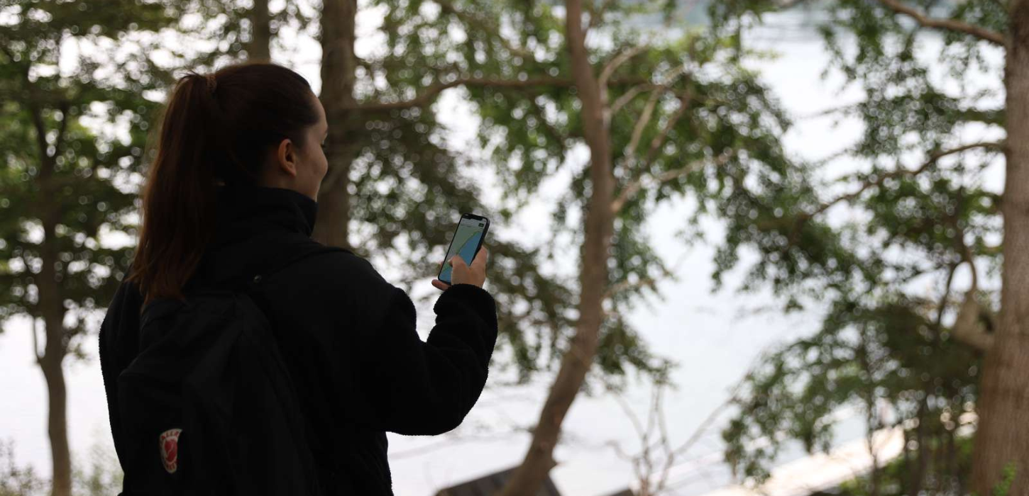 Billede af person i natur omgivelser, som holder telefon med det digitale vandrepas app åben